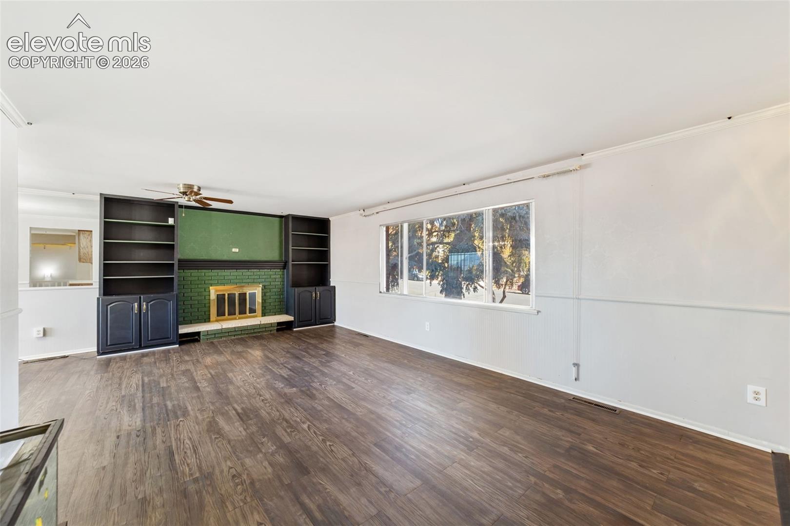 Living area featuring wood-finish flooring, a fireplace with a green tile surround, and built-in shelving units