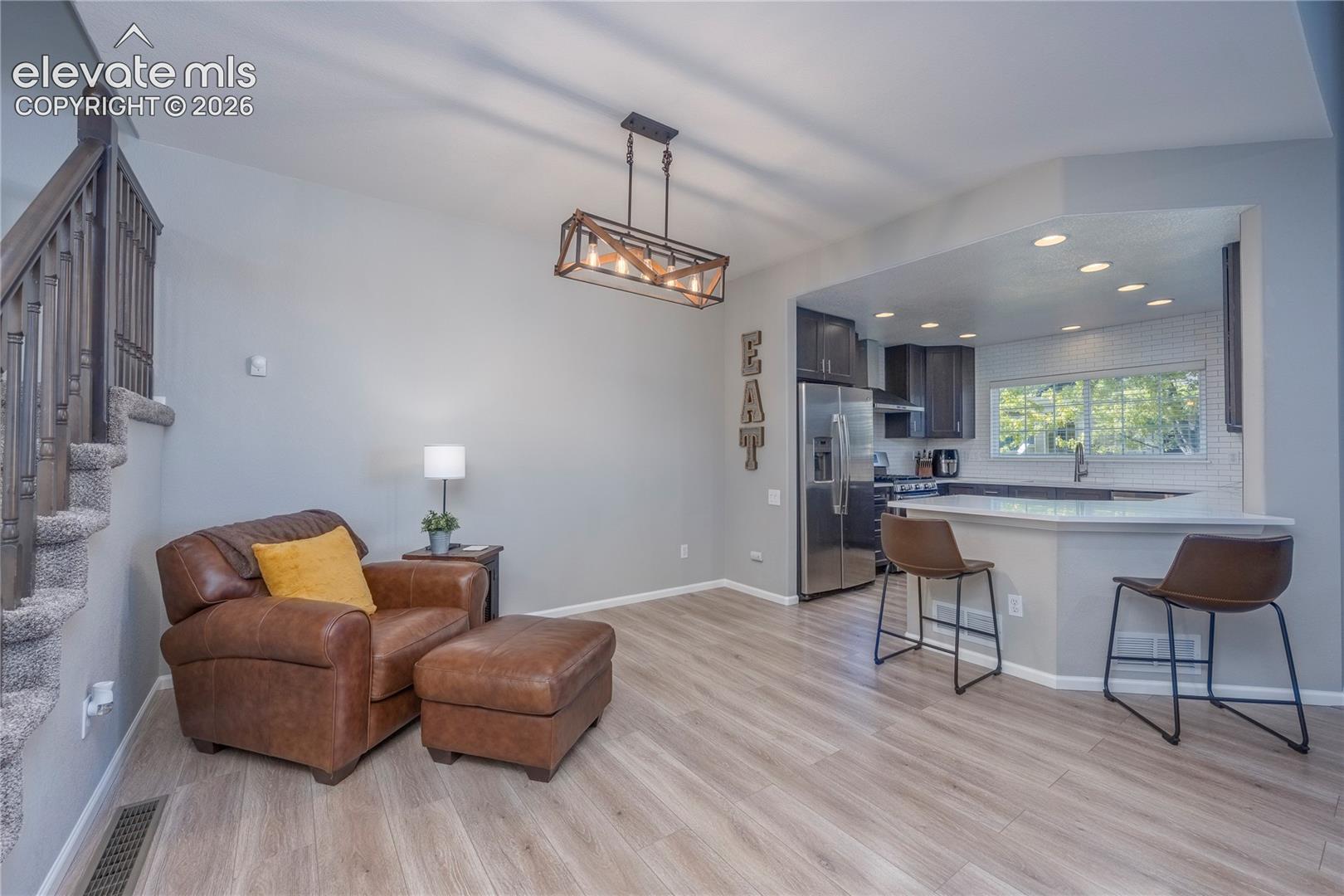 Open-concept area featuring wood-finish flooring, a kitchen peninsula with bar seating, and a rectangular multi-bulb pendant light fixture