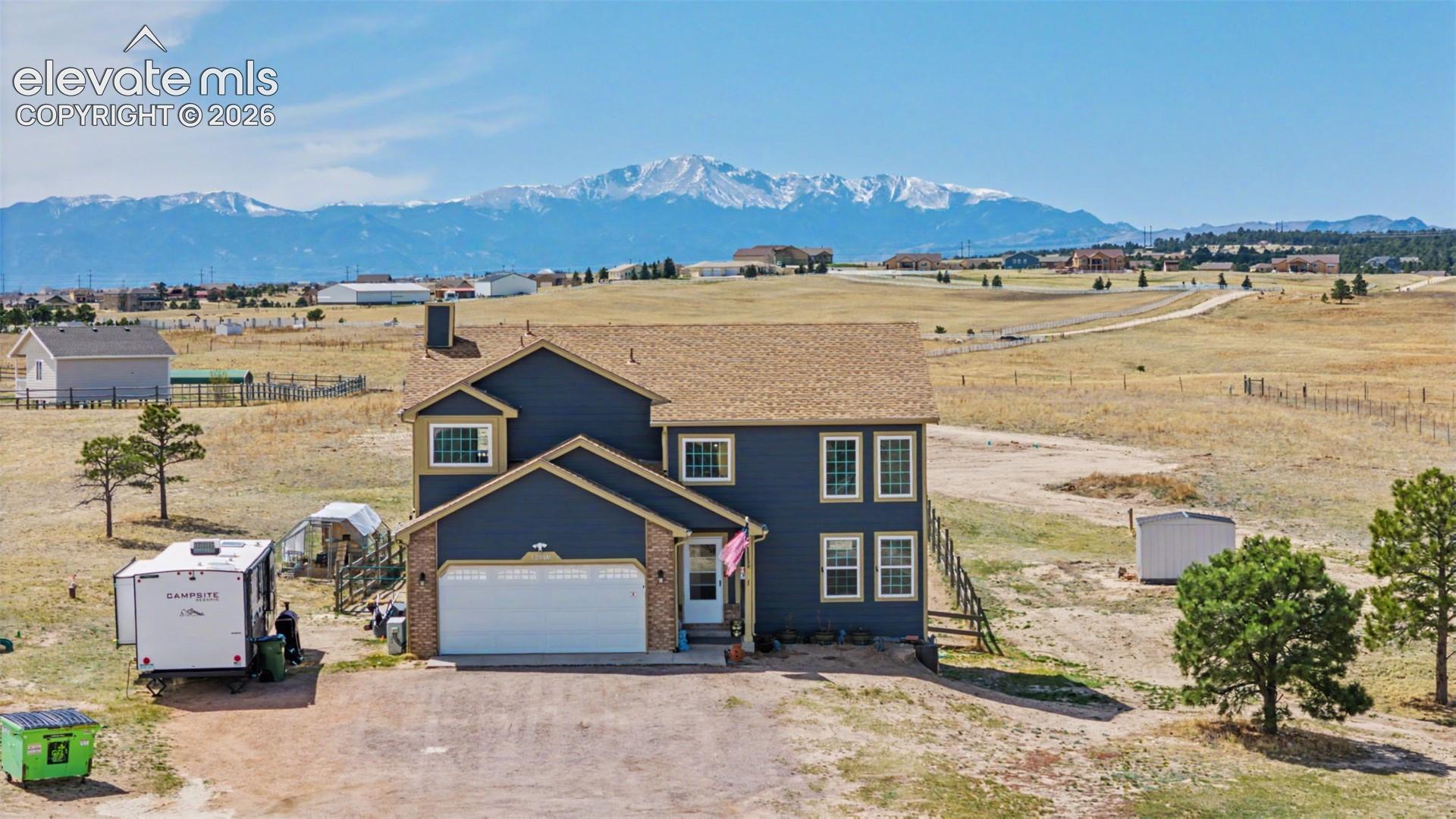 Two-story residence featuring blue siding, brick accents, a gabled roofline, an attached two-car garage, and mountain scenery