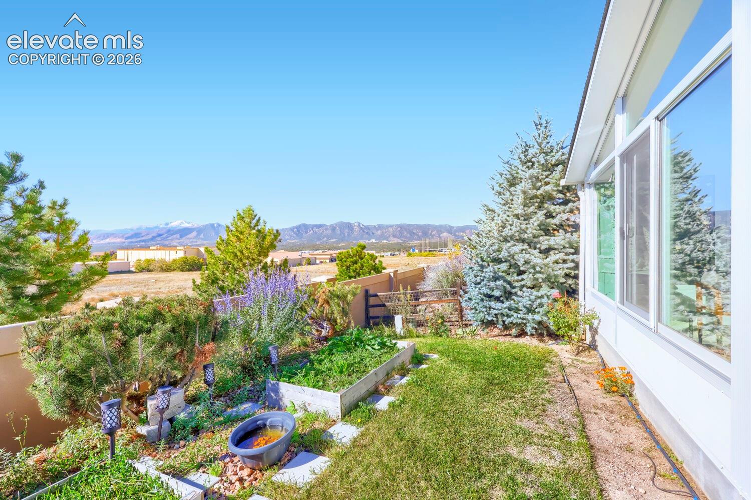 Exterior space featuring raised garden beds, manicured turf, mature evergreen landscaping, and expansive mountain scenery