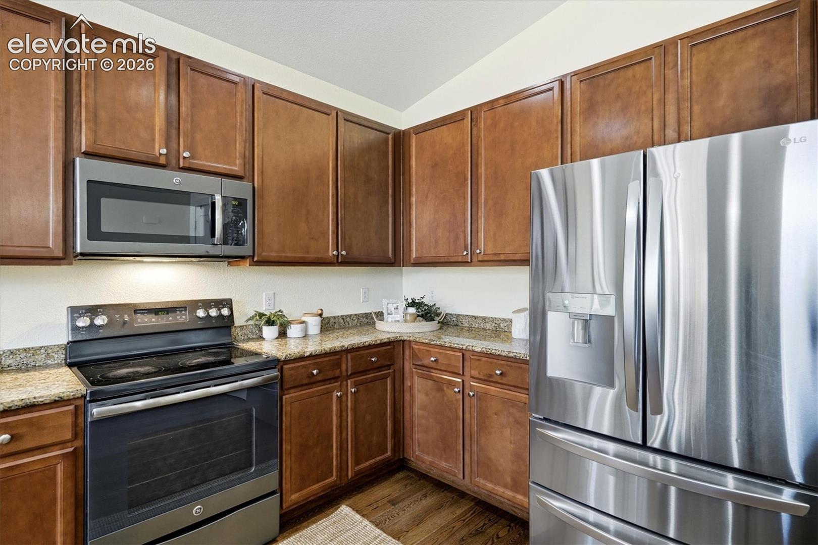 Warm wood cabinetry and stainless steel appliances anchor this well-appointed kitchen, featuring granite countertops, black electric range, over-the-range microwave, and French-door refrigerator