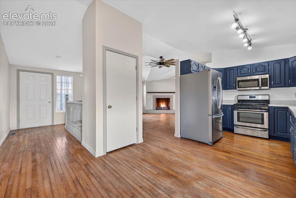 Kitchen featuring navy blue cabinetry, stainless steel appliances, wood-finish flooring, and a fireplace with a masonry surround