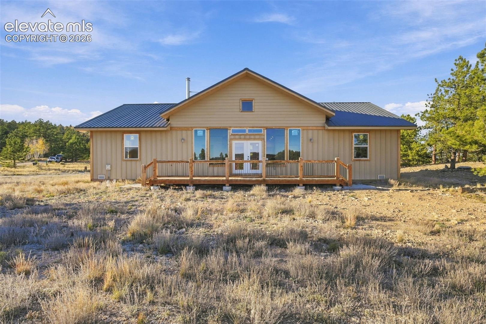 Single-story exterior with vertical siding, metal roofing, expansive glass window panels, and a wood-railing deck