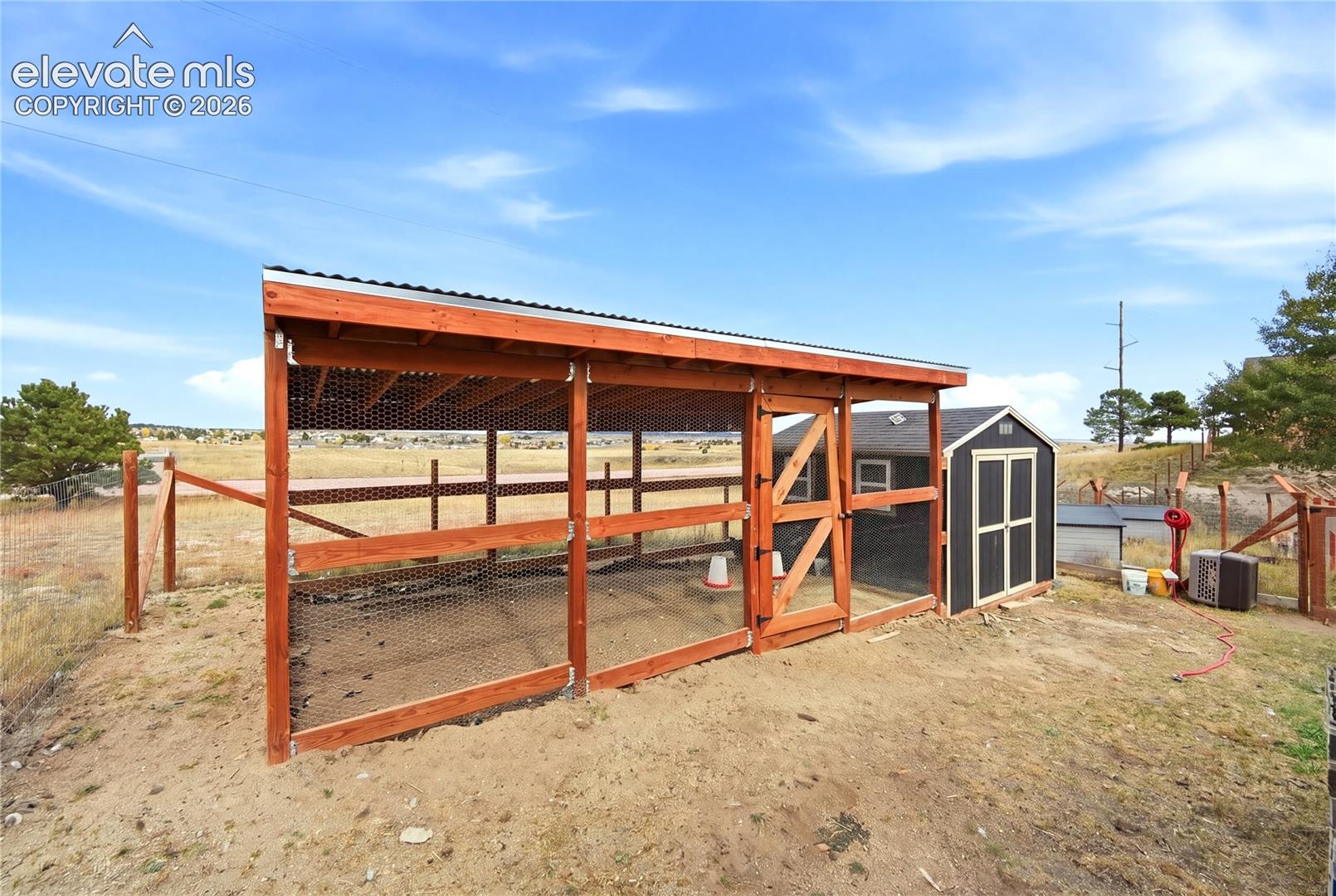 Outdoor enclosure featuring timber framing, wire mesh siding, a corrugated metal roof, and an attached storage structure