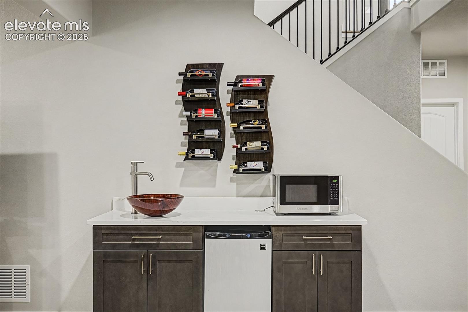 Basement wet bar features custom wine shelving, cabinetry, and a beverage refrigerator for added convenience and style.