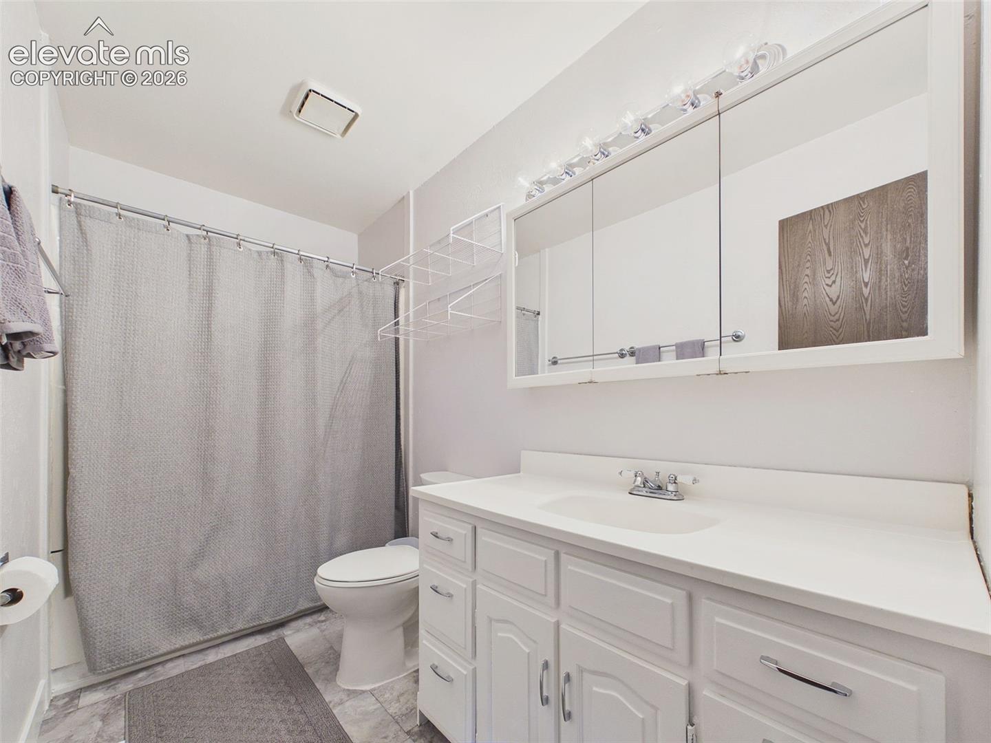 Full bathroom featuring a tub/shower combination, spacious vanity with ample counter space, mirrored medicine cabinets, and convenient wall-mounted shelving.