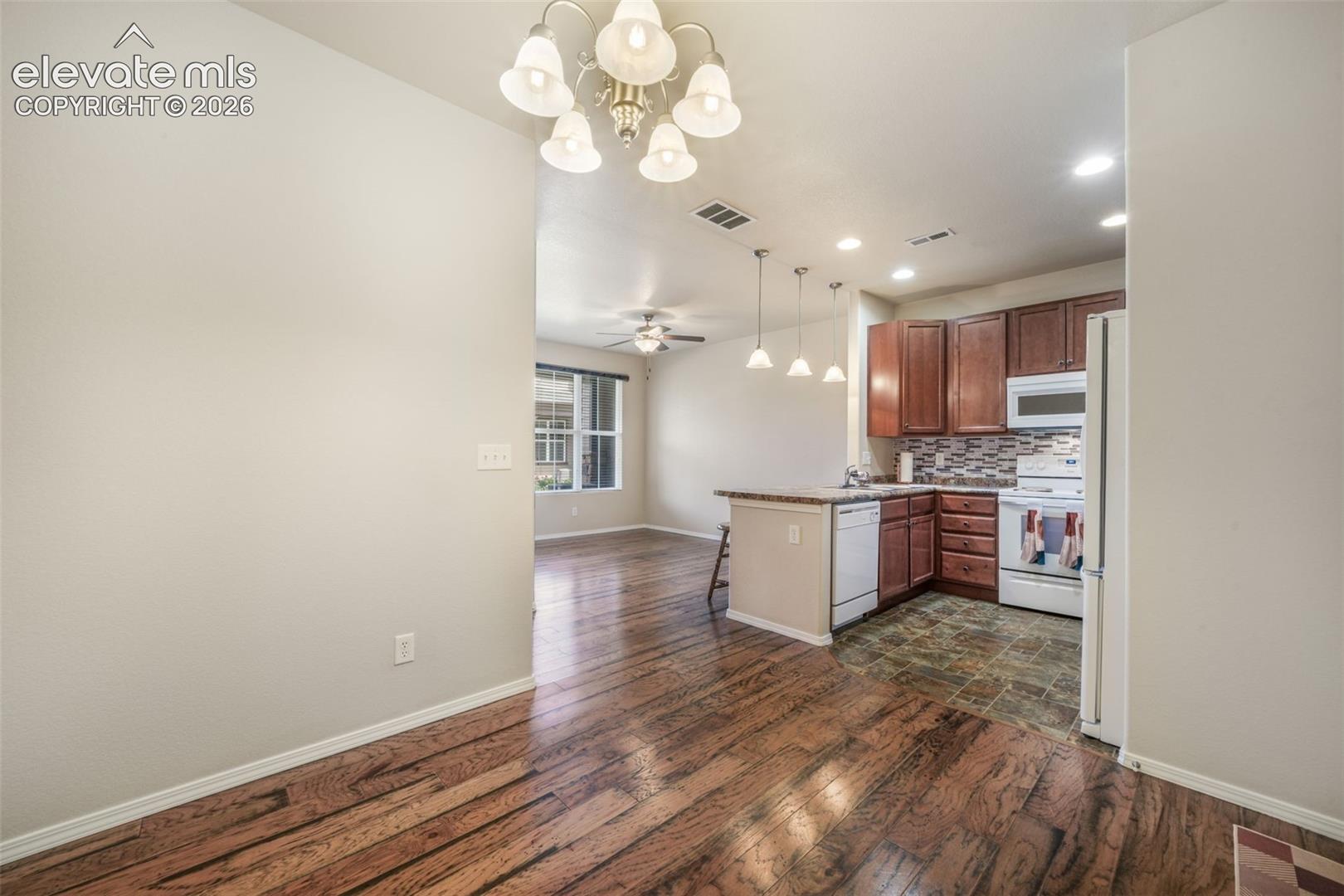 Kitchen featuring dark wood cabinetry, a tiled backsplash, and white appliances
