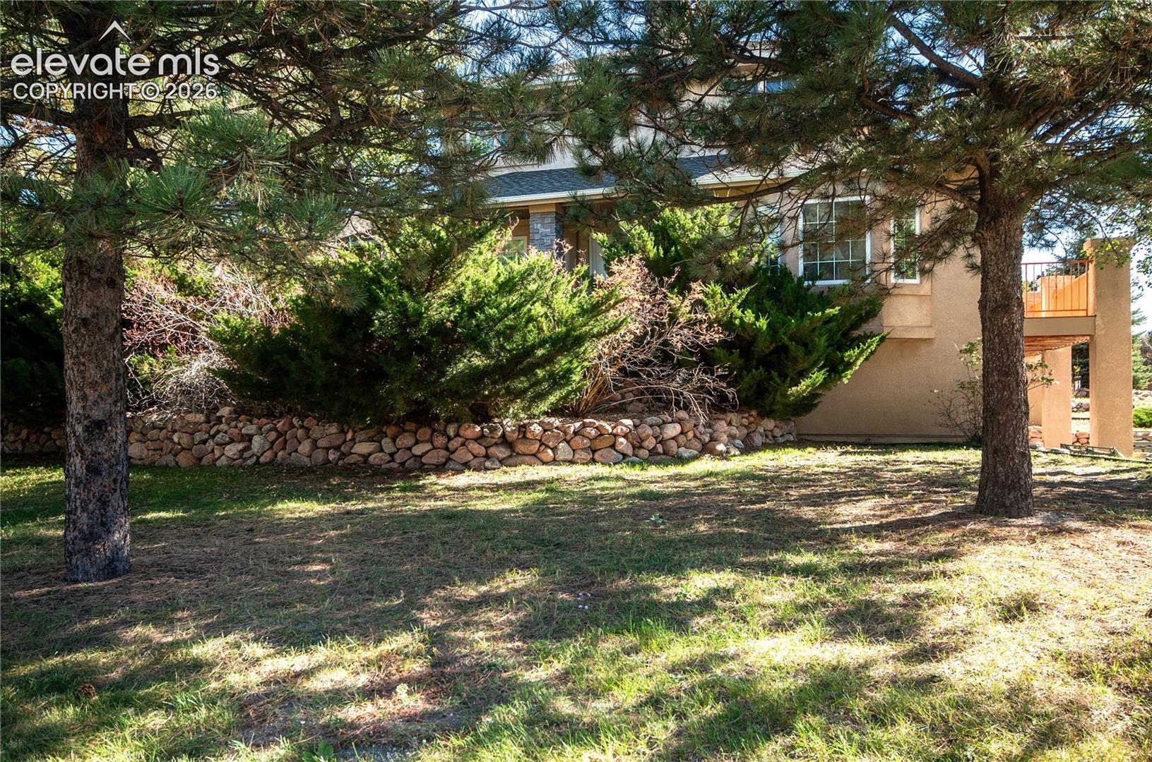 Landscaped exterior featuring mature trees, a stone retaining wall, and established shrubbery
