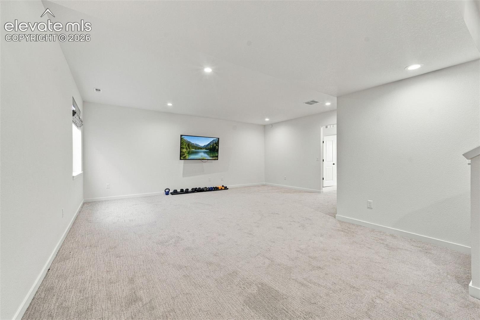 Open-concept room featuring neutral wall-to-wall carpeting, recessed ceiling lighting, and a wall-mounted television