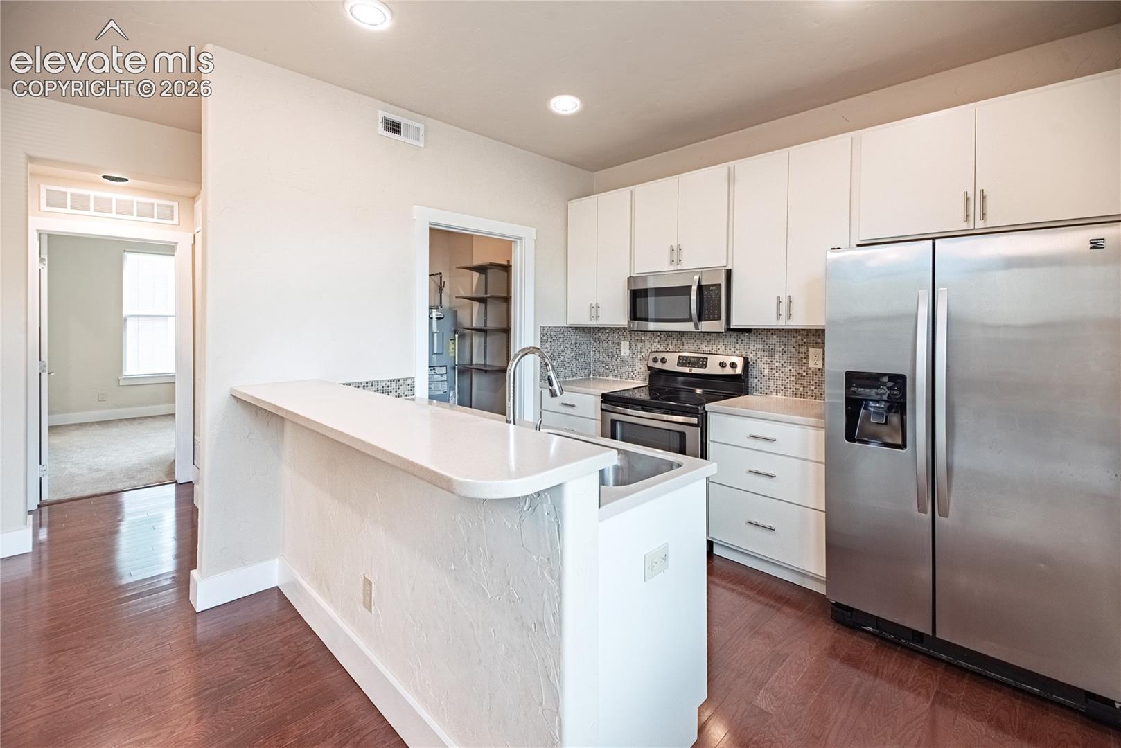 Kitchen featuring wood-finish flooring, white cabinetry, stainless steel appliances, mosaic tile backsplash, and recessed lighting