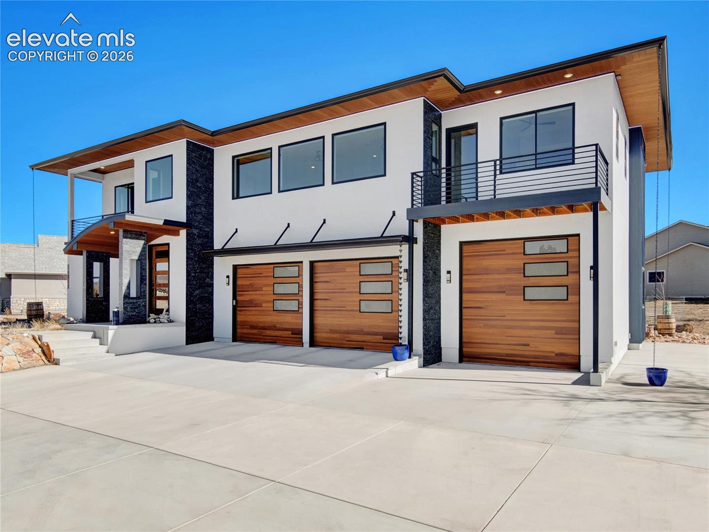 Contemporary exterior featuring crisp white stucco, dark stone accents, and warm wood-finish garage doors