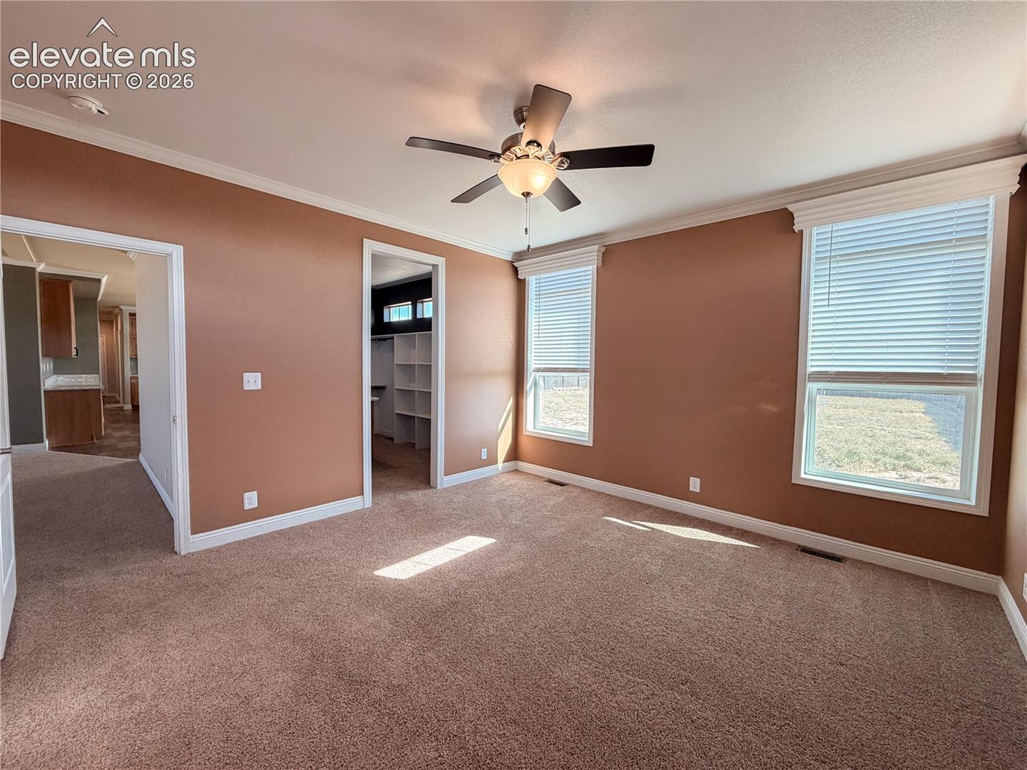 Neutral wall finishes featuring carpeting, crown molding, double-pane windows with horizontal blinds, and a central ceiling fan with integrated lighting