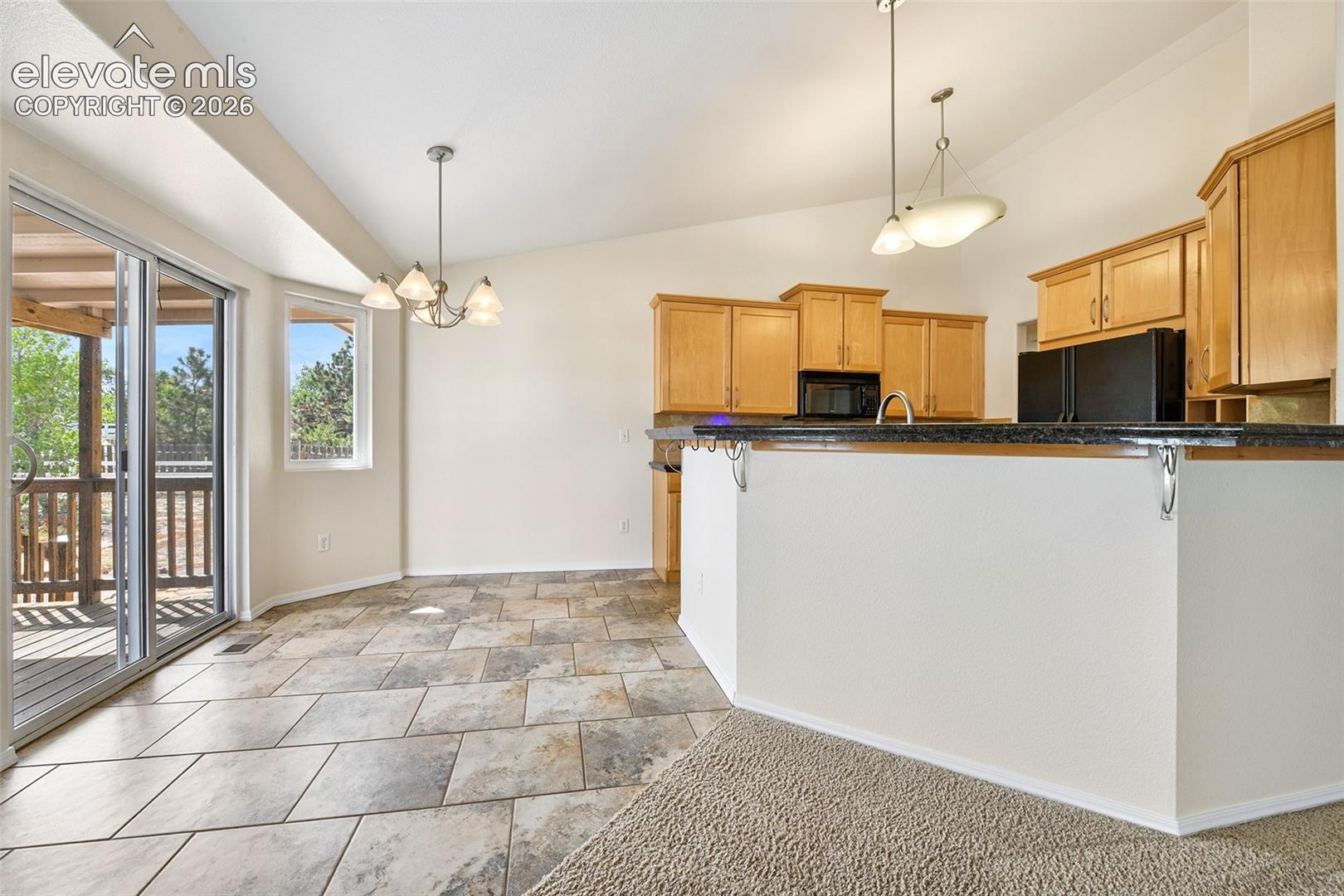 Vaulted ceilings, a full kitchen with wood cabinetry, and sleek black appliances