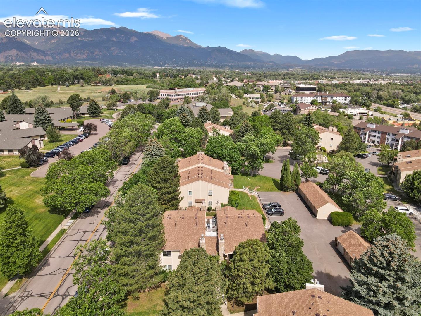 Arial view showing the roof top of 850(front and center in this photo taken in the summer) the a/c units are visible, parking area is shown on the right of the photo and Tenderfoot Hill Road is on the left.  Also shows the mature tree and landscaping and the nearby mountain backdrop