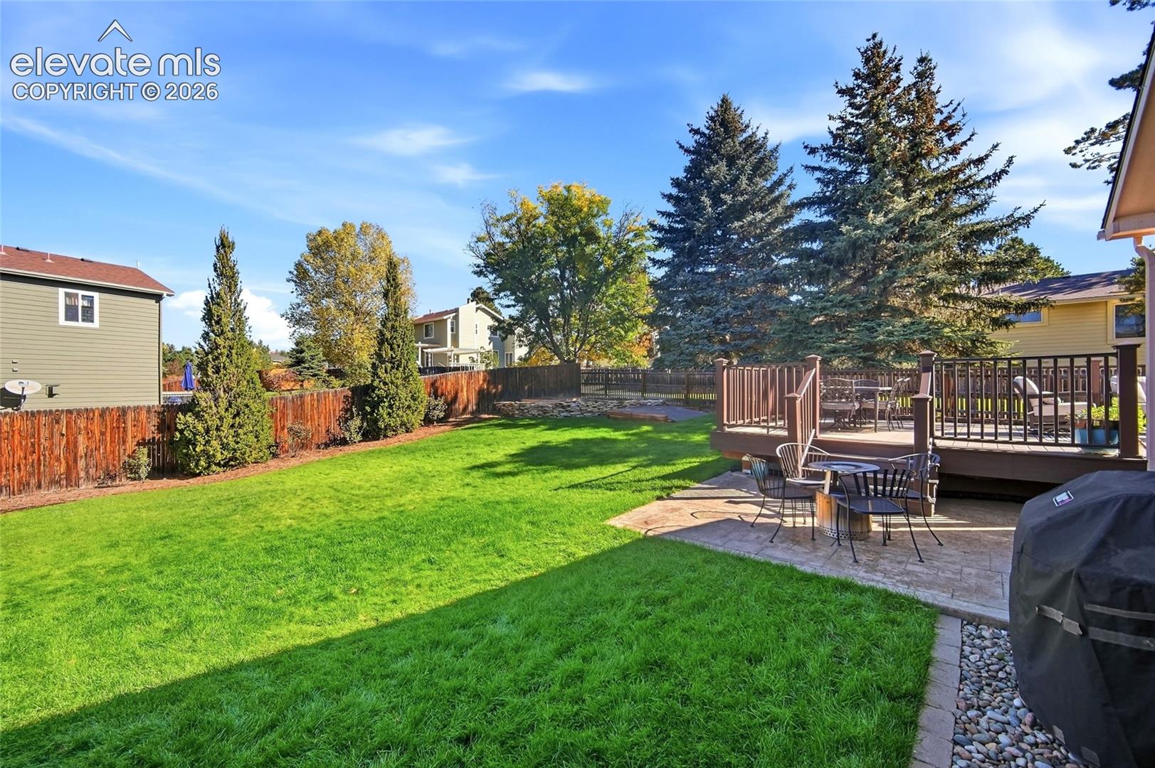 Expansive backyard featuring a large green lawn, wood privacy fence, and mature trees