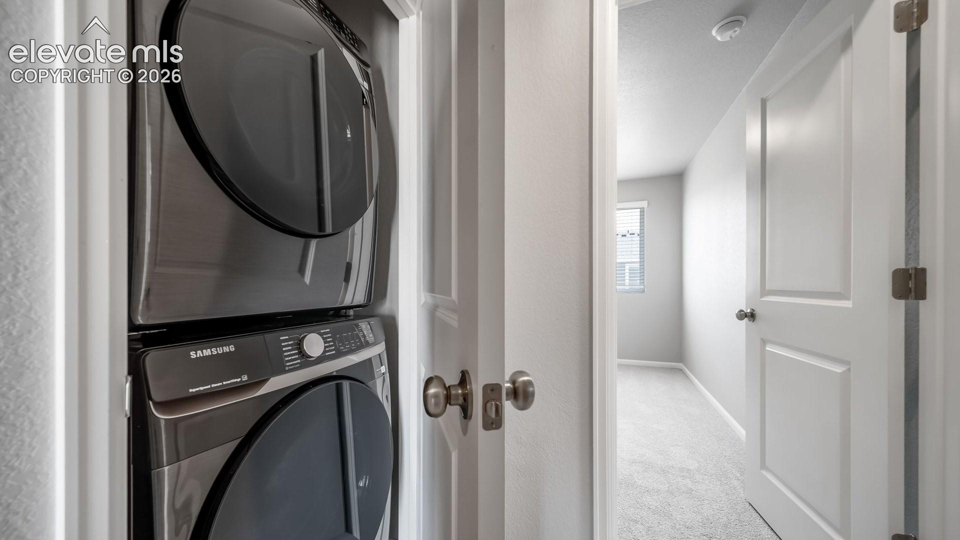 Stacked stainless steel laundry appliances situated within a dedicated closet featuring neutral wall finishes and paneled interior doors
*photos of a model home*