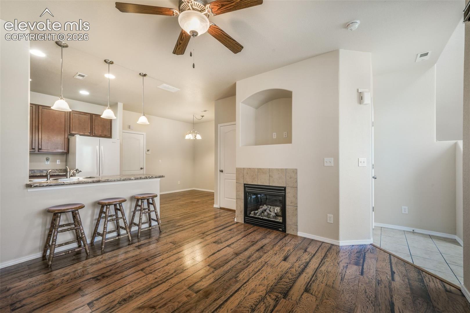 Wood-finish flooring, built-in fireplace with tile surround, ceiling fan, and pendant lighting