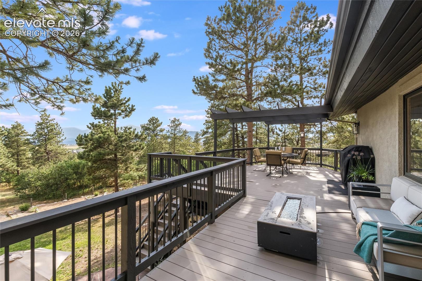 Expansive outdoor deck featuring wood-finish flooring, dark-stained railings, a pergola, and mountain scenery