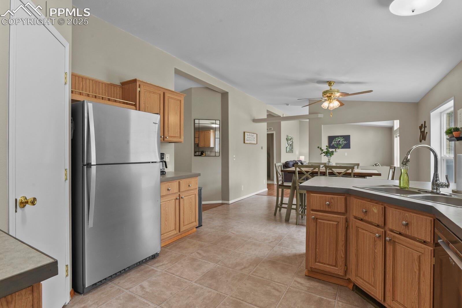 Kitchen with stainless steel appliances, vaulted ceiling, a ceiling fan, brown cabinetry, and light tile patterned floors