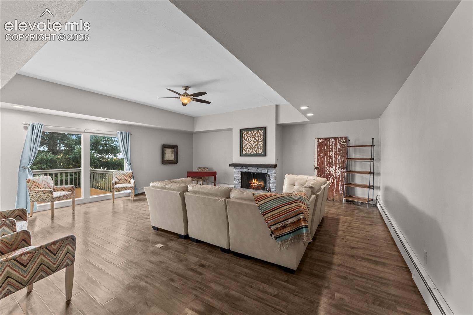 Open-concept living space featuring vaulted ceilings, wood-finish flooring, a stone-surround fireplace, and large sliding glass doors providing access to an exterior deck