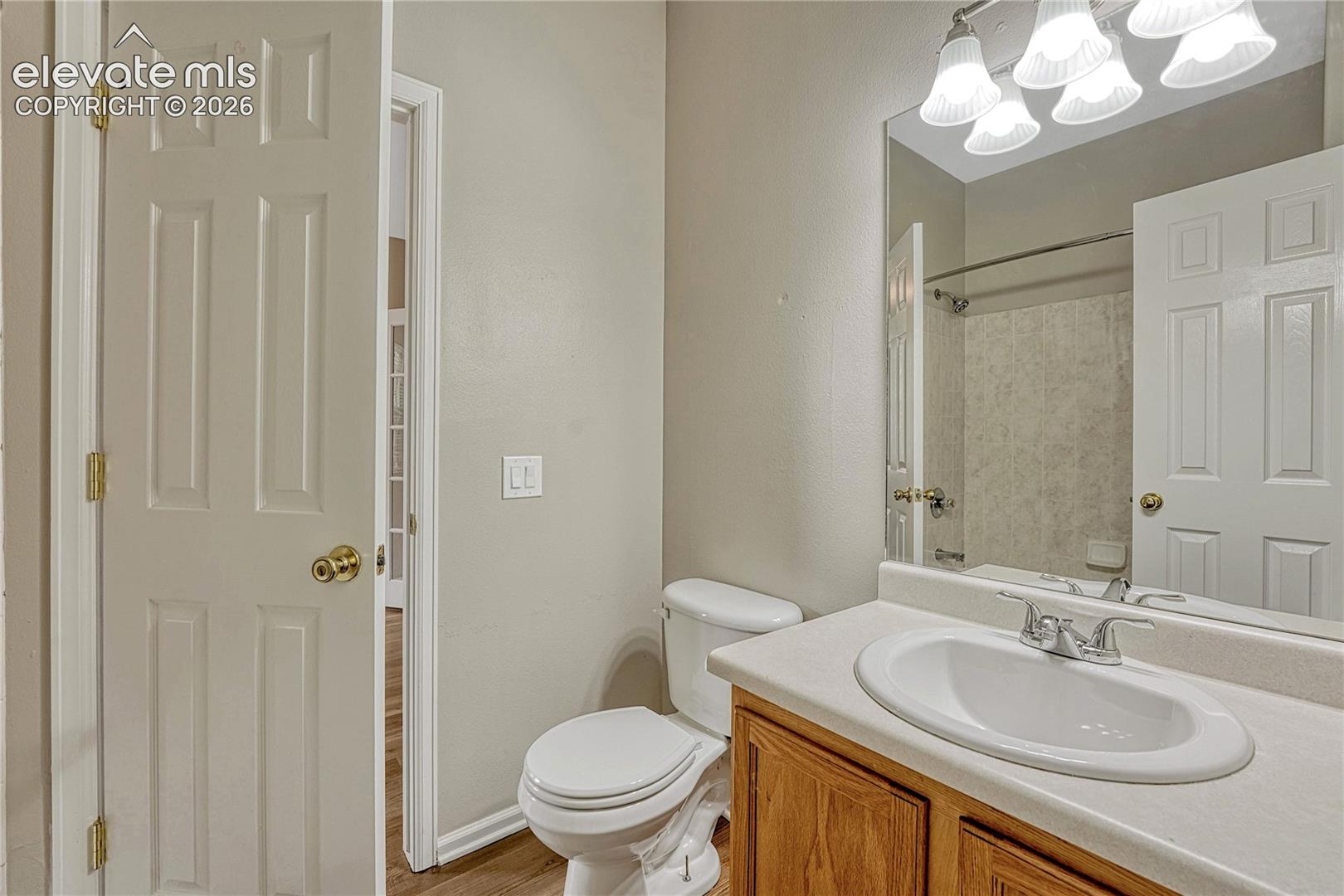 Bathroom featuring a vanity with a white integrated sink and countertop, wood-finish cabinetry, wall-to-wall mirror, and multi-light overhead fixture