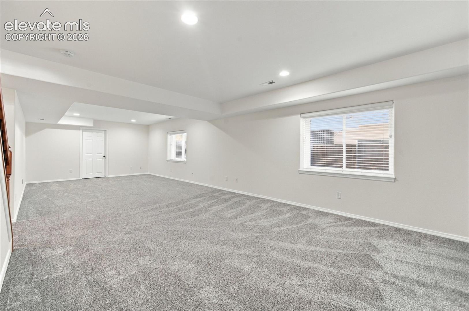 Open-concept interior featuring neutral wall paint, wall-to-wall carpeting, recessed ceiling lighting, and multiple windows with installed blinds