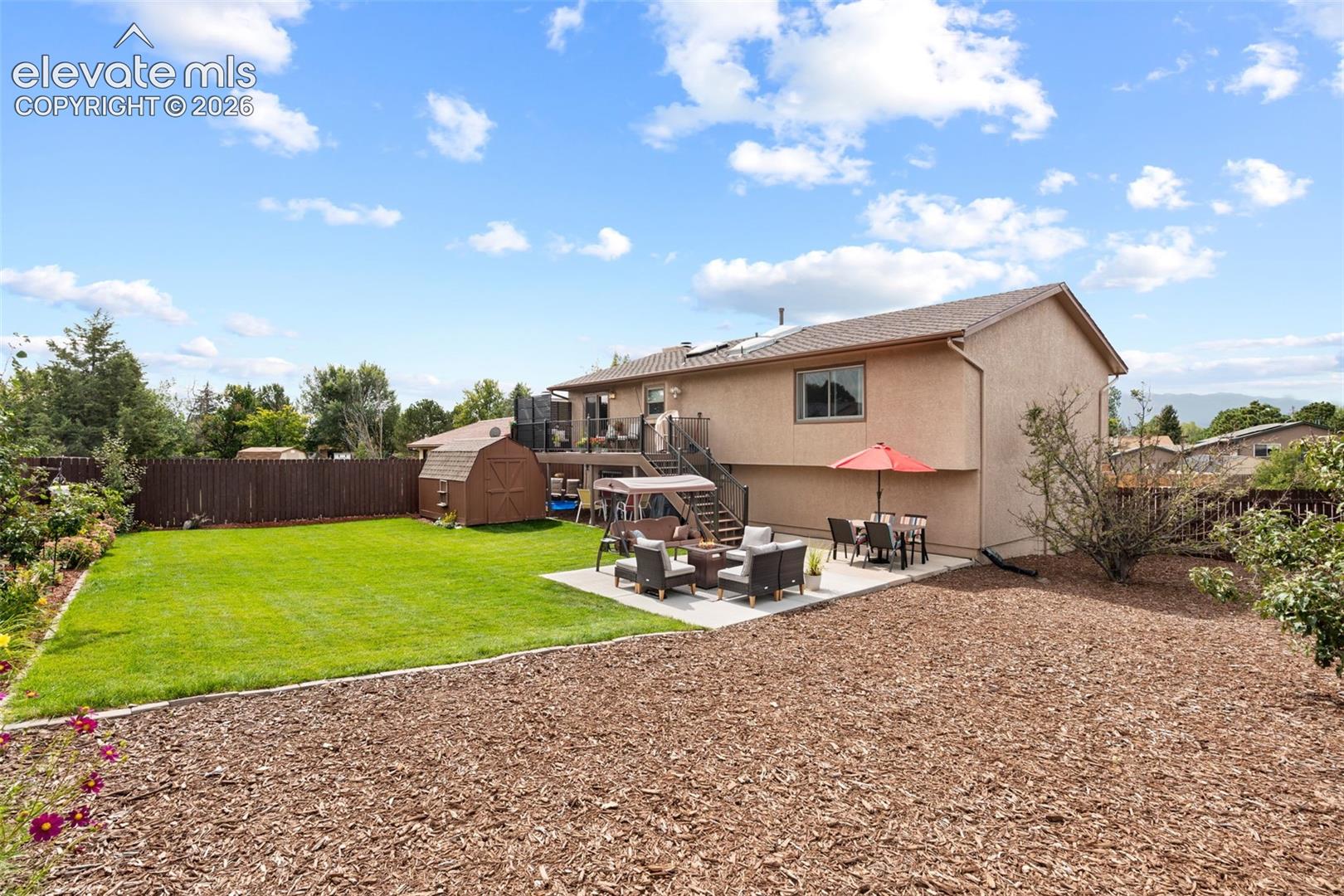 Fenced backyard featuring a manicured lawn, concrete patio, elevated deck with metal railing, and a storage shed