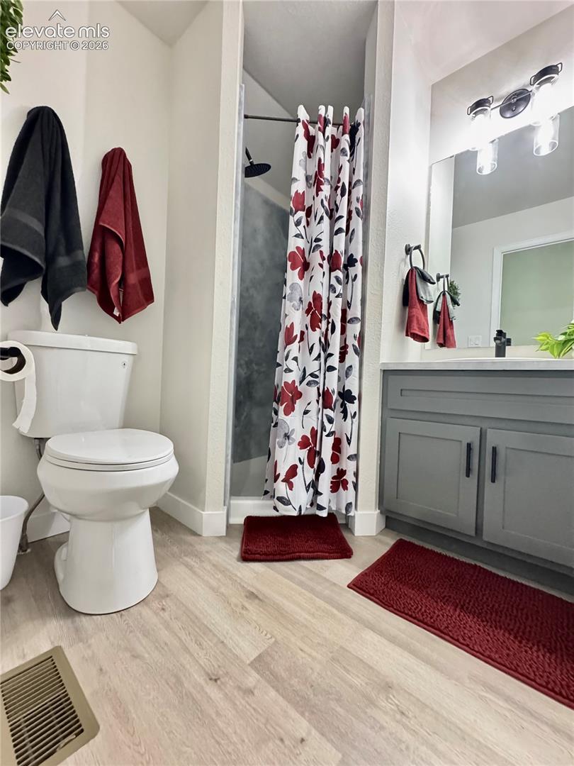 Grey shaker-style vanity with rectangular sink, stone-finish countertop, matte black hardware, and light wood-finish flooring