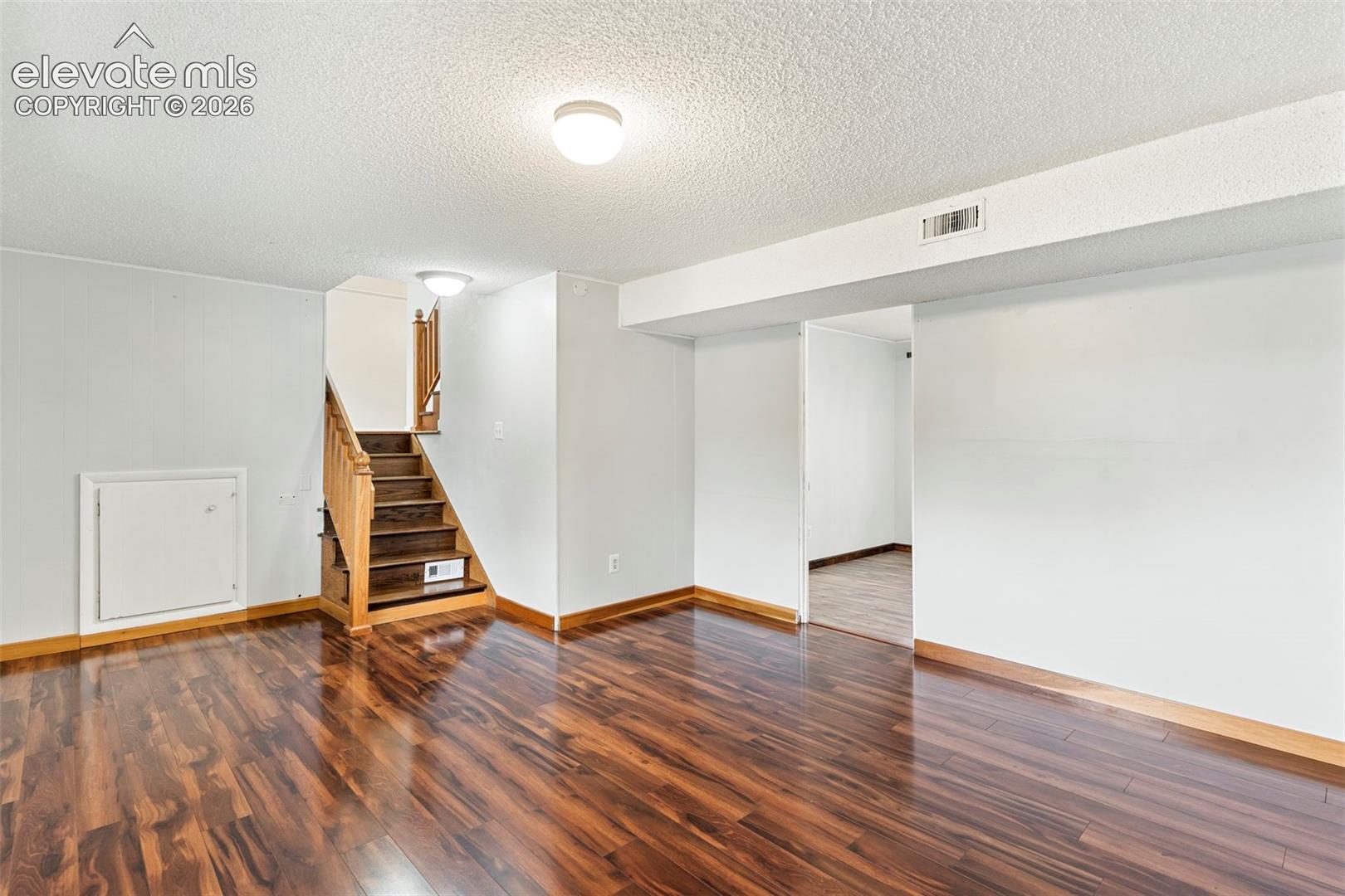 Wood-finish flooring with coordinating wood trim, staircase with wood handrails, and flush-mount ceiling lighting
