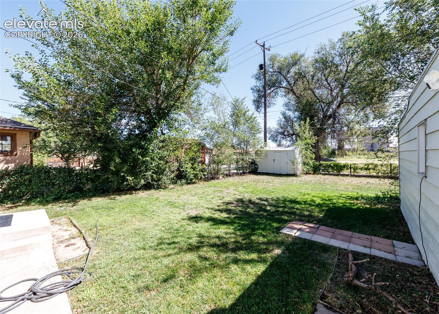 Expansive yard featuring a grass lawn, mature trees, and a storage shed