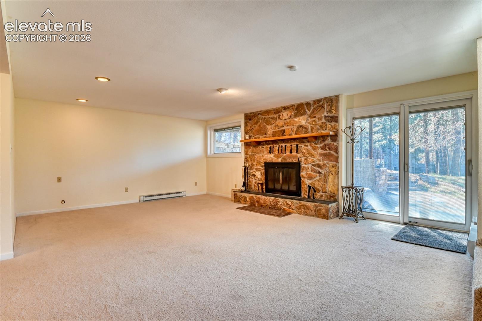 Family room featuring a floor-to-ceiling stone fireplace, natural wood mantel, recessed lighting, and sliding glass door providing access to the front yard. 