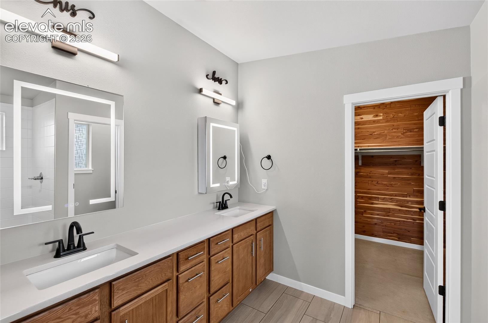 Adjacent to Master Bedroom and walk in closet Double vanity with integrated sinks, light-toned countertops, and wood-finish cabinetry