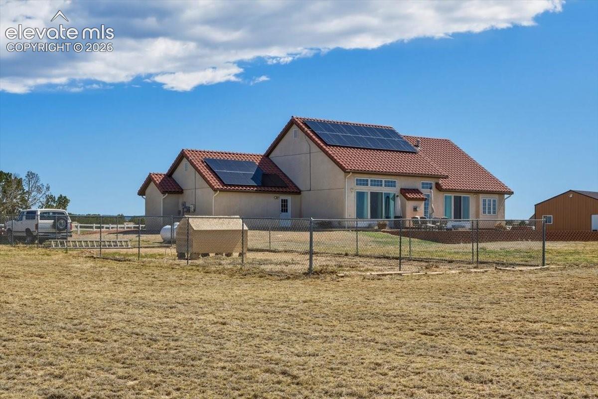 Rear view of the home showcasing solar panels, outdoor living space, and a fenced area ideal for animals, hobbies, or flexible outdoor use.