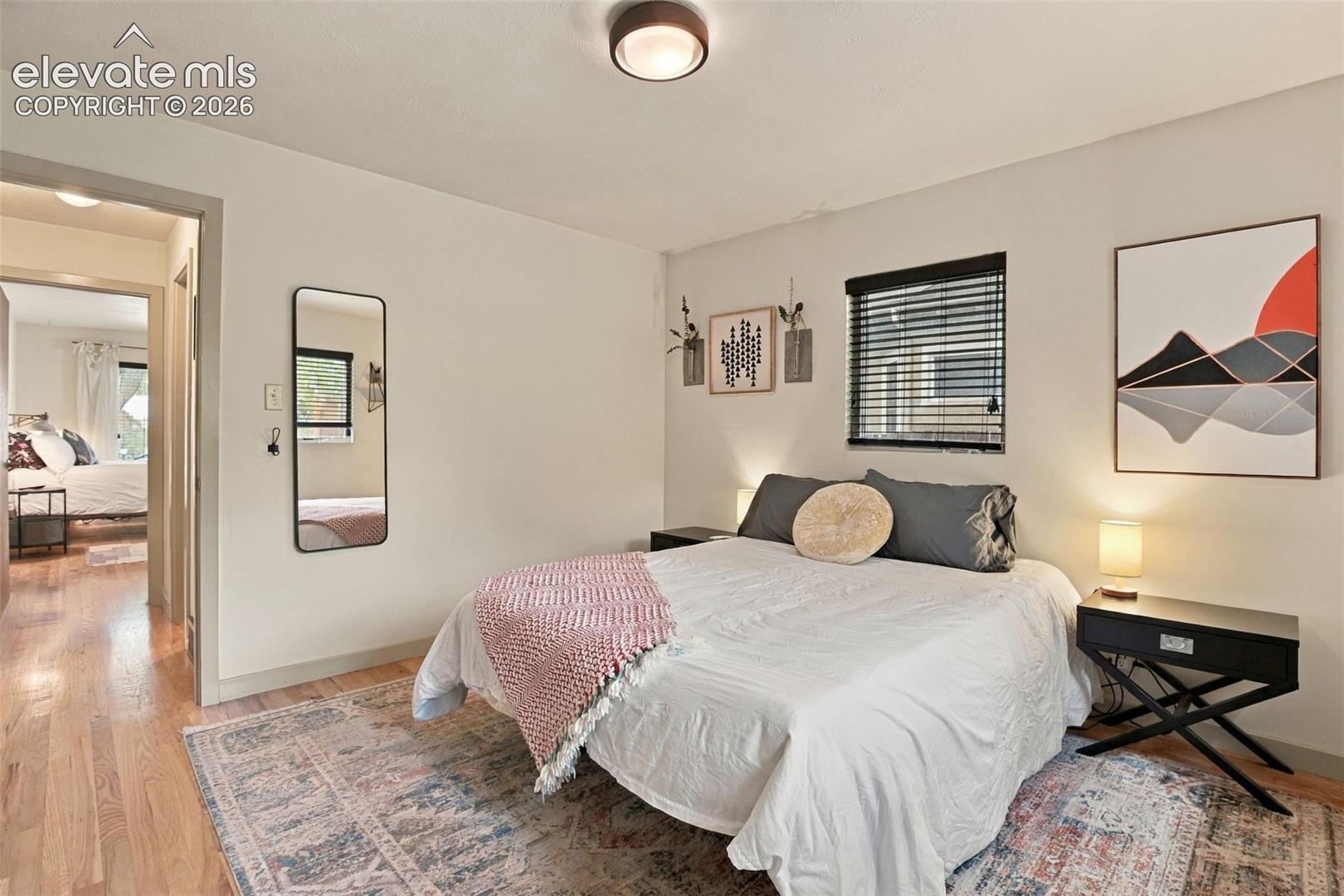 Bedroom featuring wood-finish flooring, a flush-mount ceiling light fixture, and a window equipped with horizontal blinds