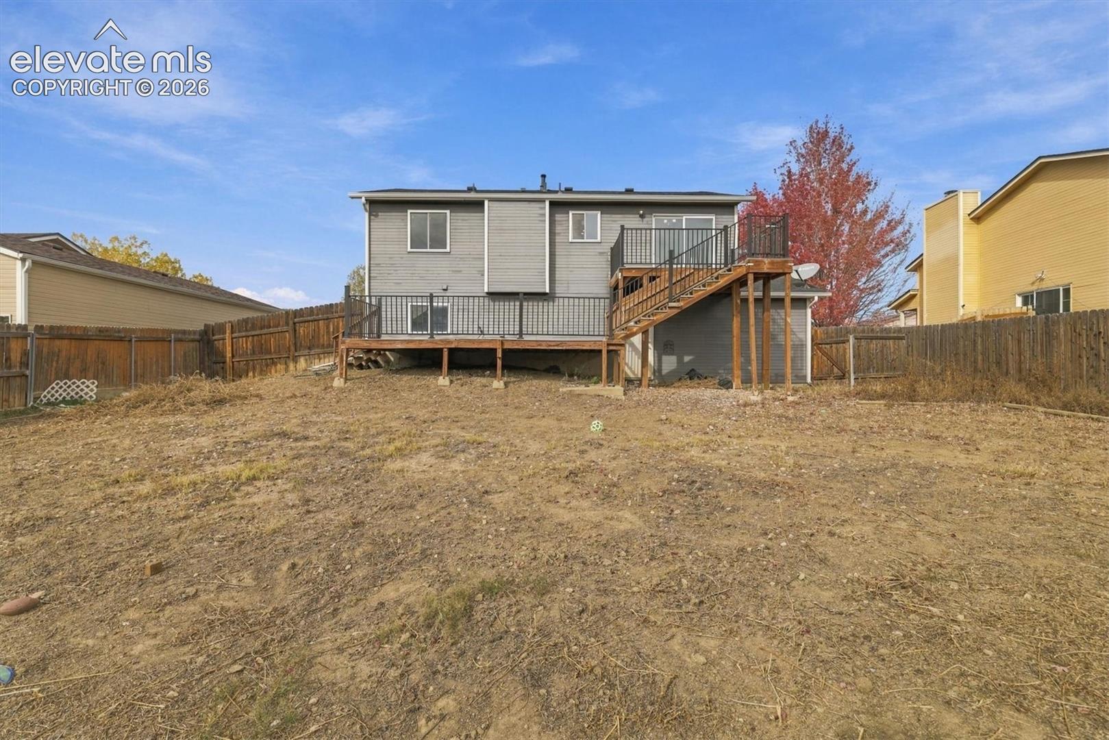 Rear exterior featuring gray horizontal siding, elevated wood deck with black metal railing, and wood privacy fencing