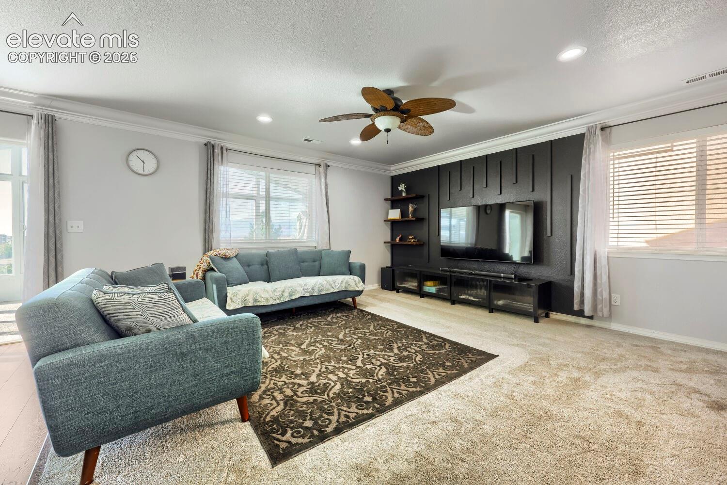 Living area featuring a black vertical slat accent wall, integrated floating shelving, recessed lighting, crown molding, and a ceiling fan with leaf-shaped blades