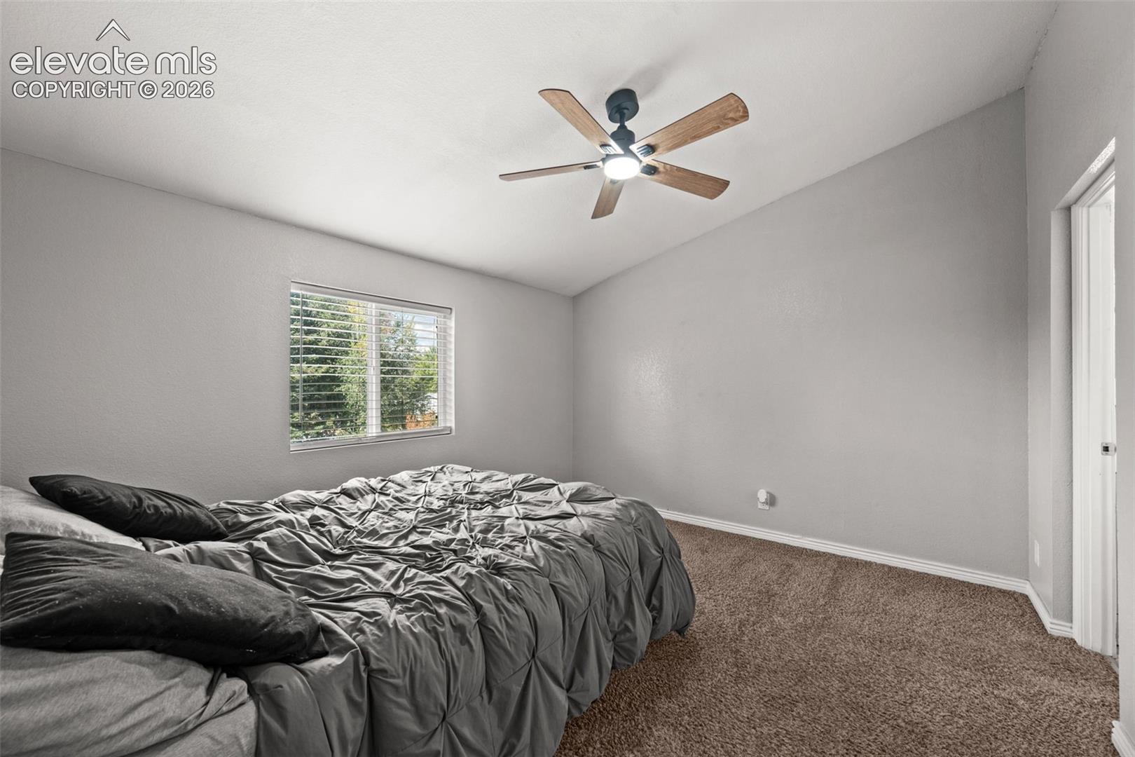 Vaulted ceiling, neutral wall tones, carpeted flooring, and a central ceiling fan with integrated lighting
