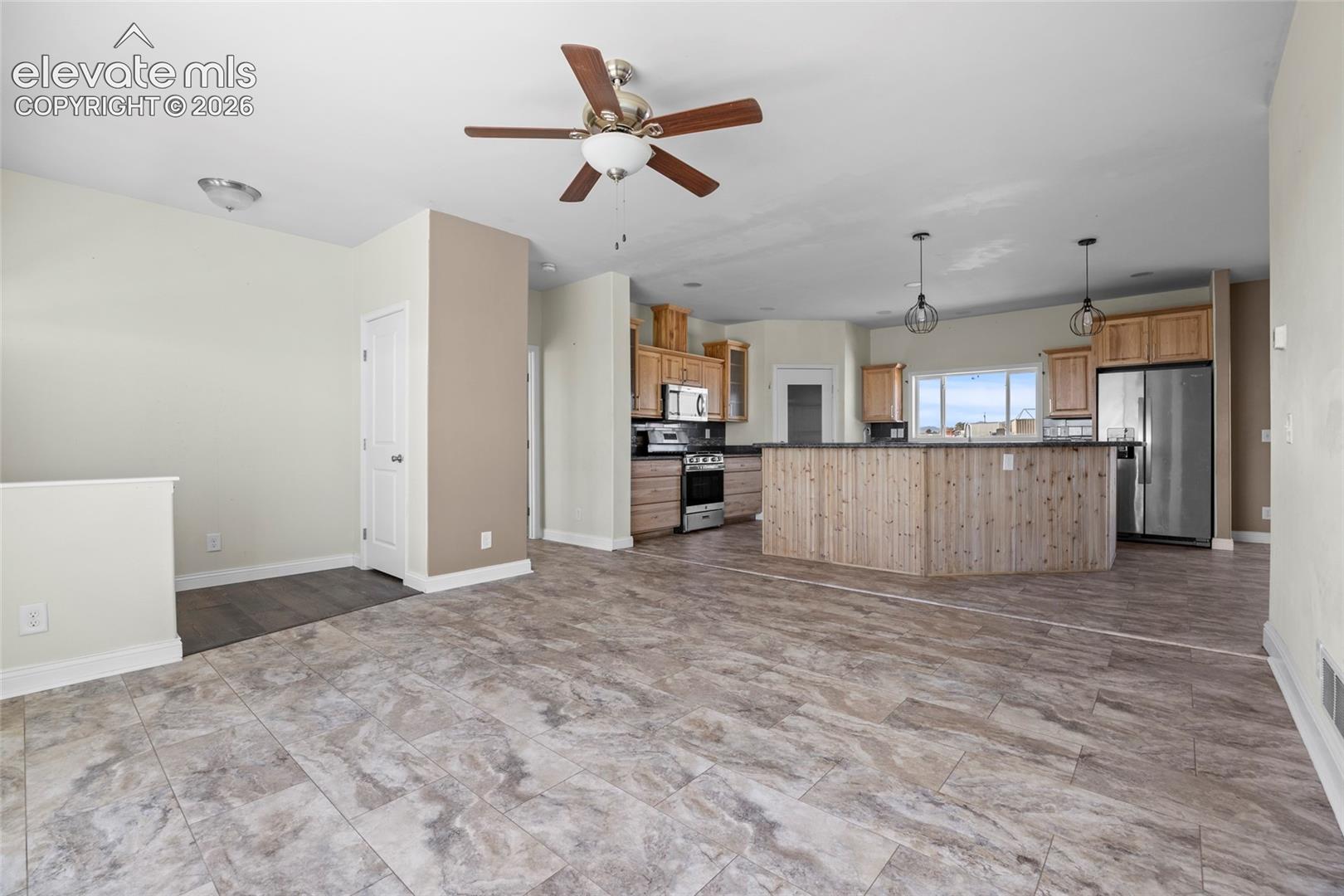 Open-concept interior featuring tile flooring, a kitchen island with wood-panel siding, stainless steel appliances, pendant lighting, and a ceiling fan