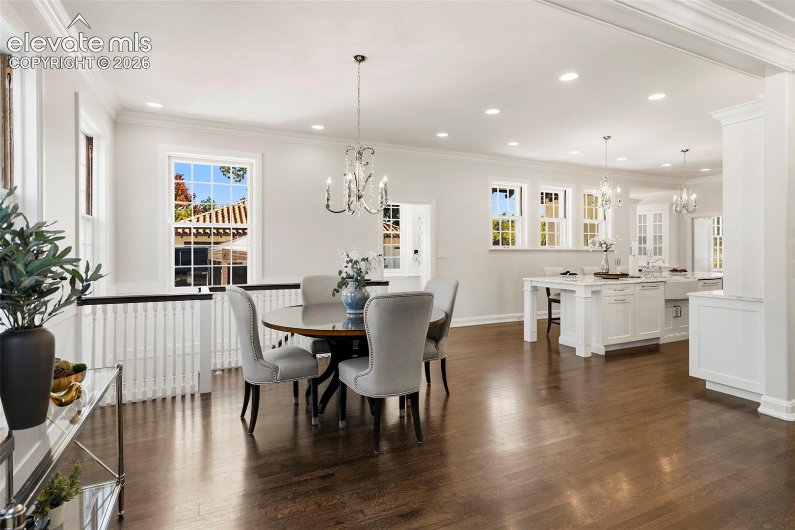 Open-concept interior featuring wood-finish flooring, multi-pane windows, recessed lighting, crown molding, and white shaker-style kitchen cabinetry with a central island