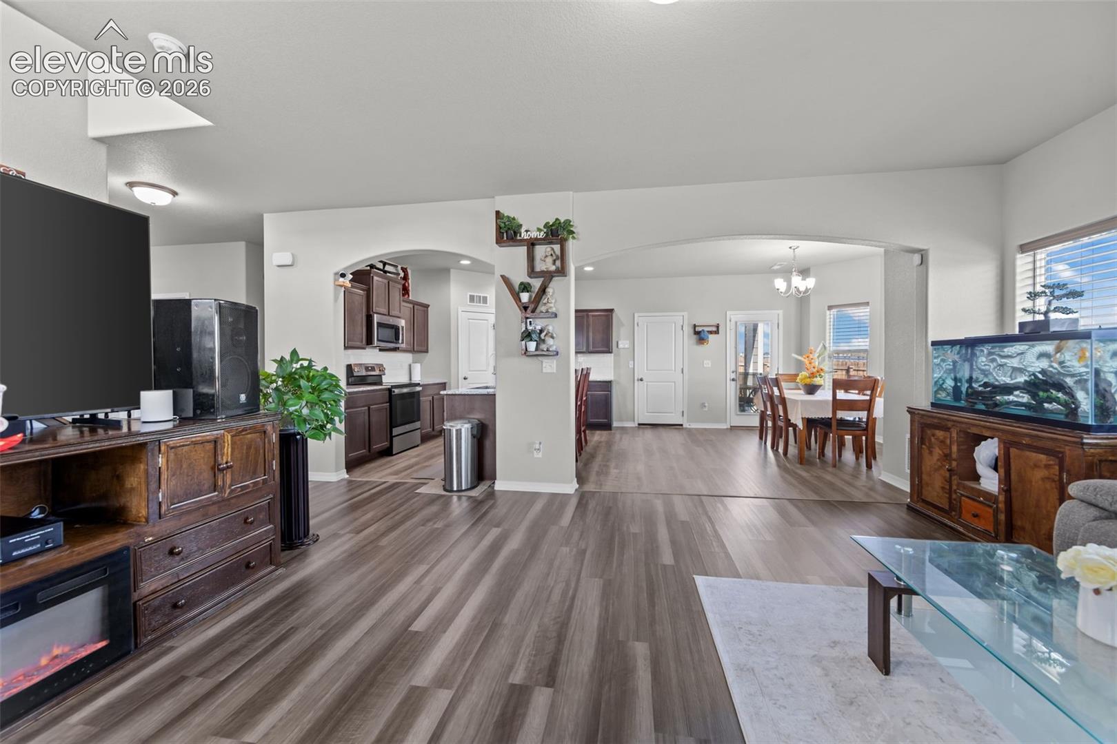 Spacious living area with wood-finish flooring, arched doorways, an open-concept kitchen, and a dining area with natural light