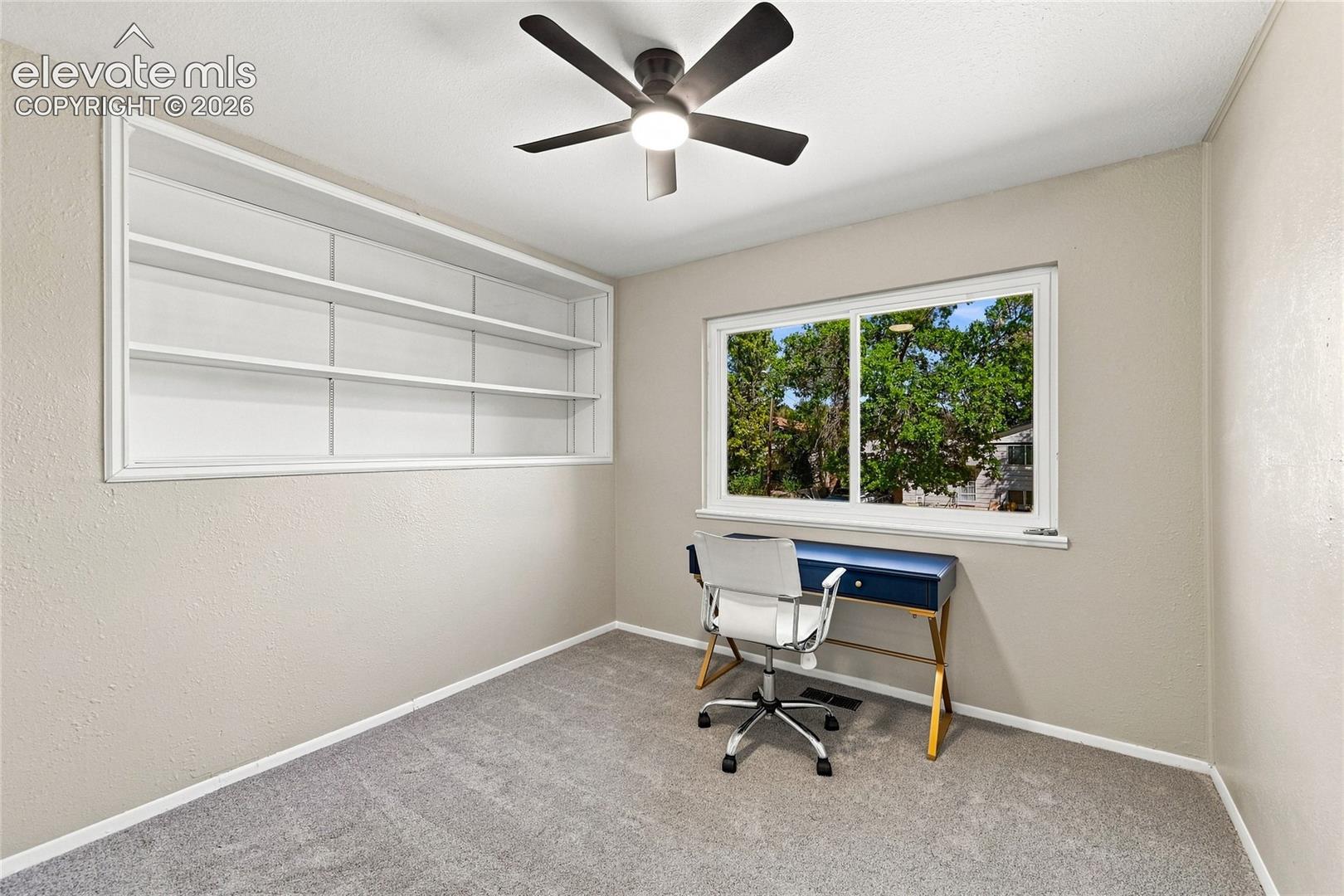 Built-in shelving, ceiling fan with integrated lighting, window with exterior scenery, and carpeted flooring