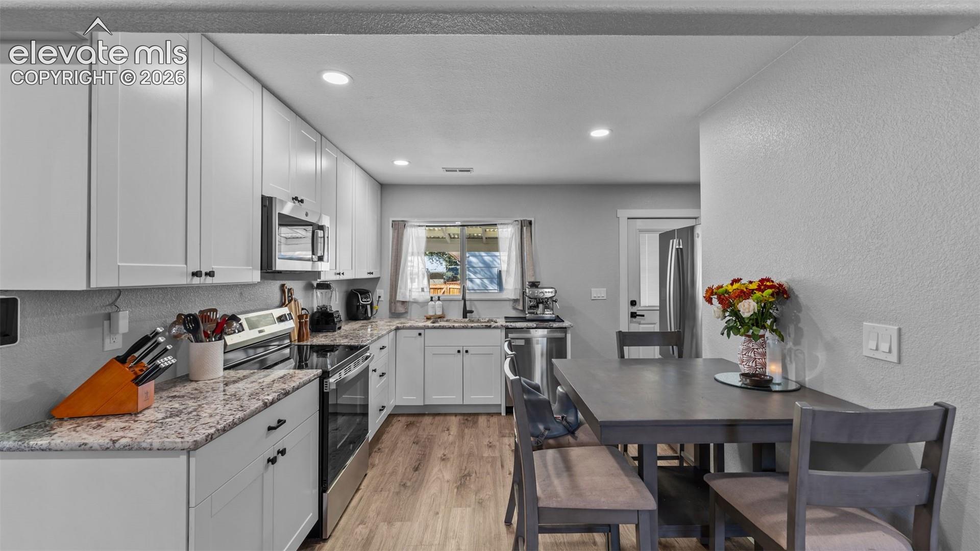 Kitchen featuring white shaker-style cabinetry, patterned stone-finish countertops, stainless steel appliances, and wood-finish flooring