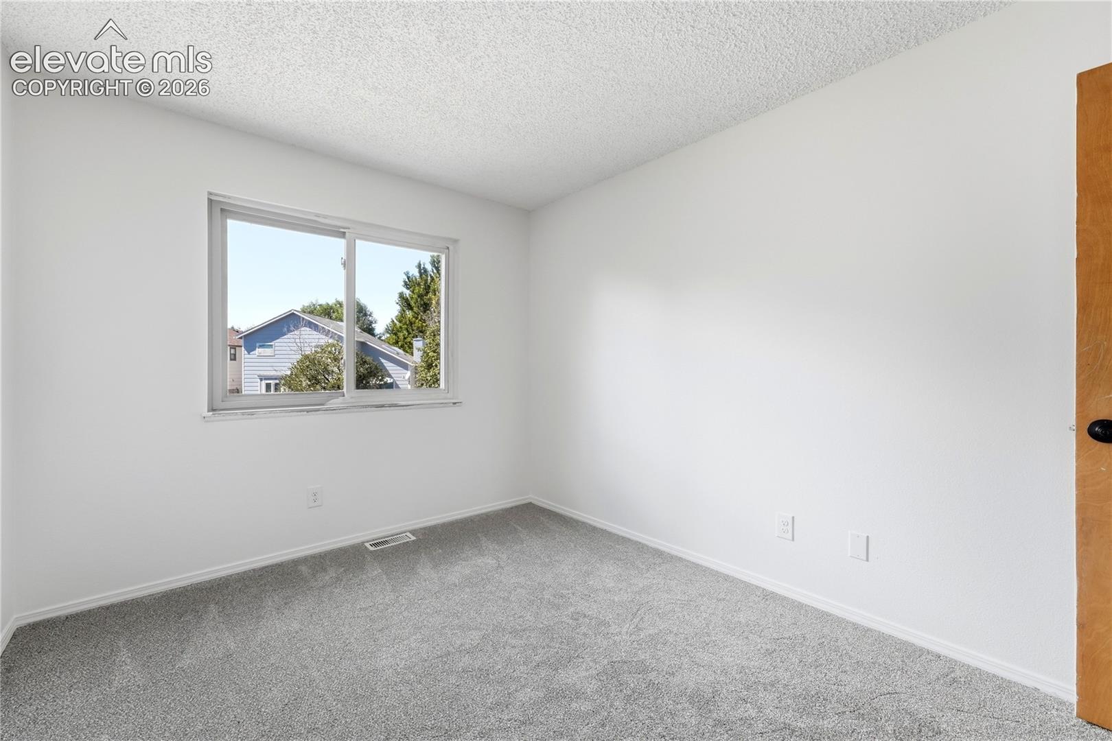 Wall-to-wall carpeting in a neutral tone, white painted walls, and a single sliding window