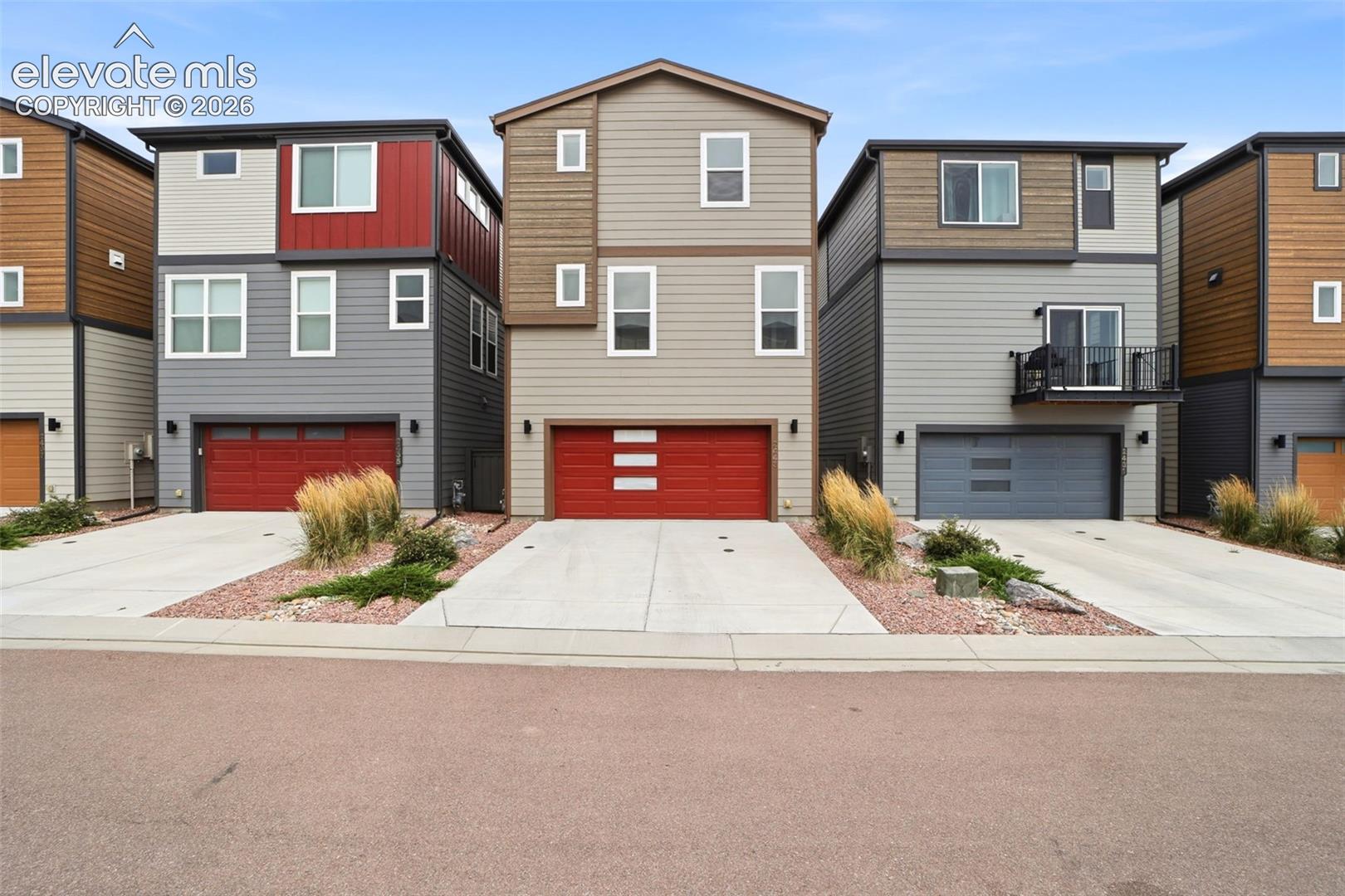 Contemporary three-story exterior featuring multi-toned siding, a red garage door, and a concrete driveway