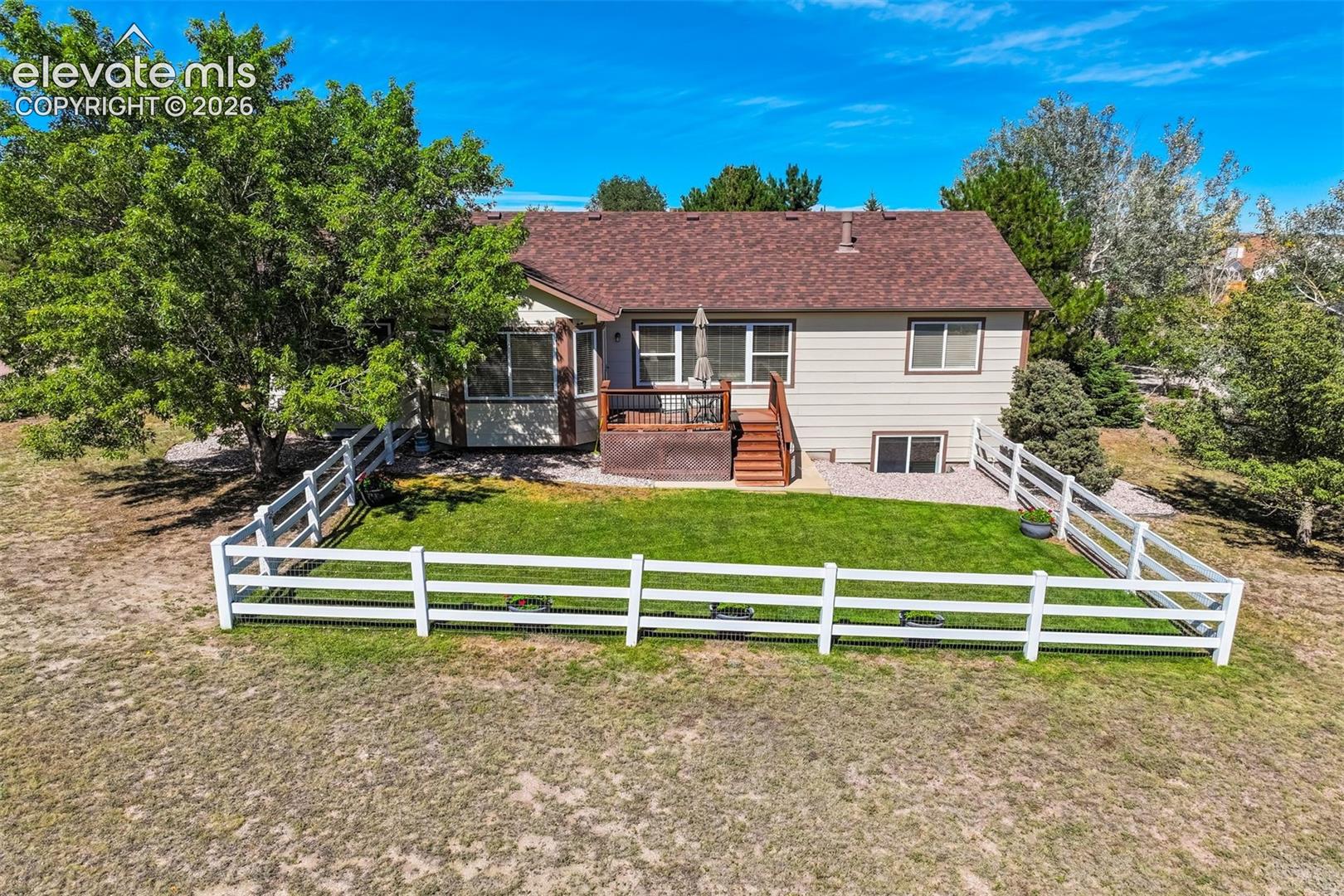 Fenced backyard featuring a manicured lawn, wood-finish deck with stairs, mature trees, and siding exterior