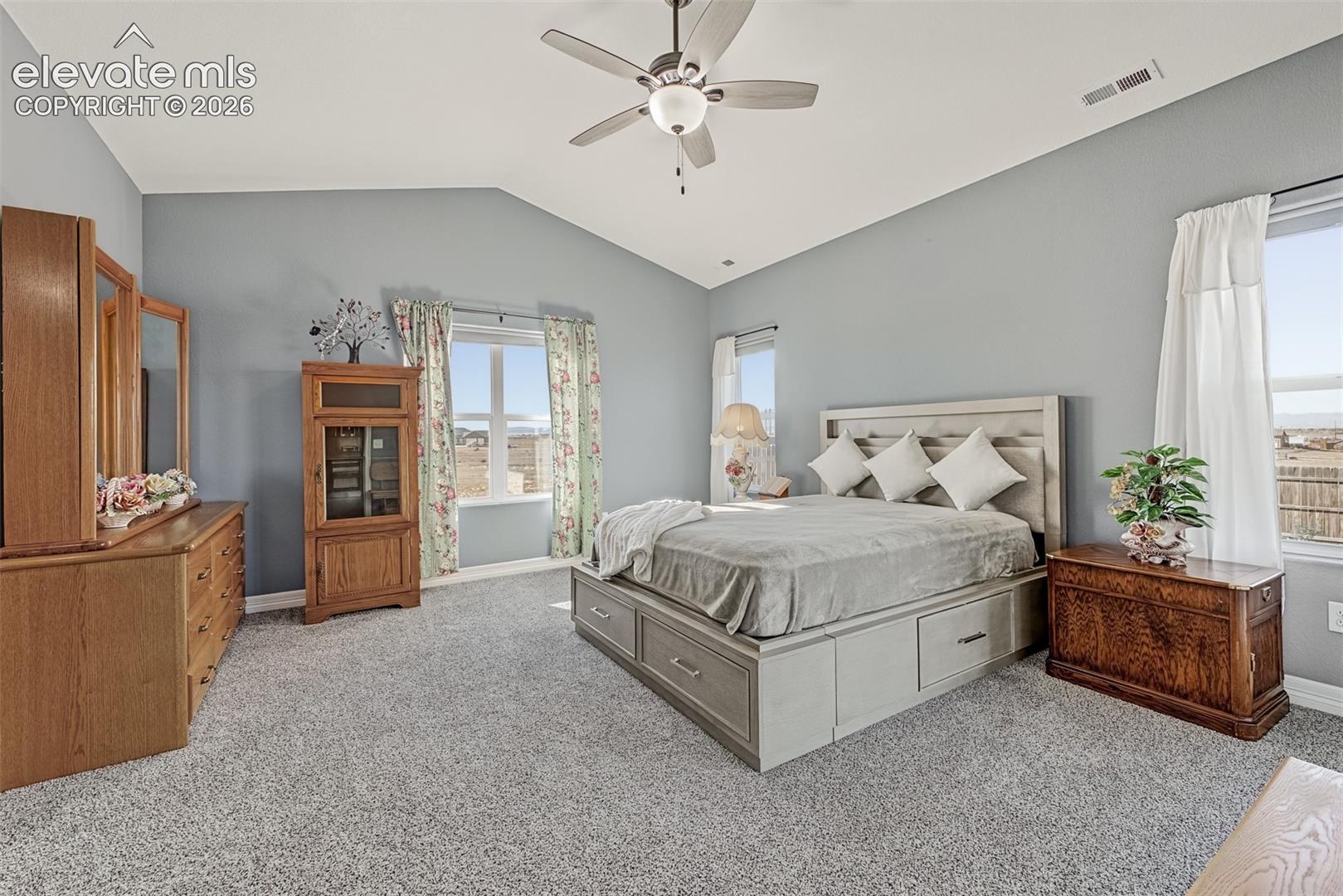 Oversized primary bedroom with newer carpet, vaulted ceilings, ceiling fan and a slider to the covered patio.