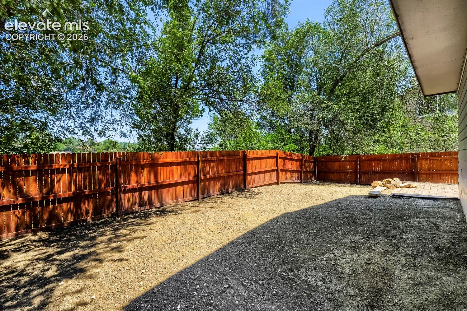 Spacious backyard featuring a full perimeter wooden fence, mature trees, and a paved patio area