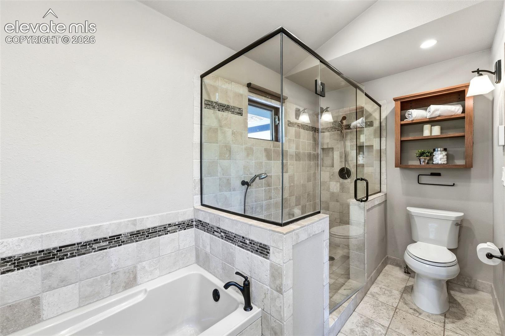 Tiled shower with glass enclosure, recessed niches, and matte black fixtures