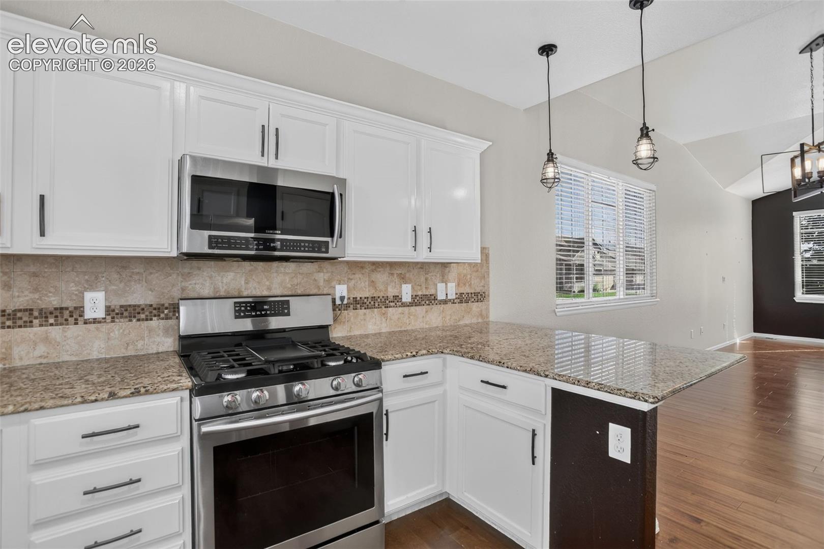 White cabinetry, stainless steel appliances, granite countertops, tile backsplash with mosaic accents, and wood-finish flooring