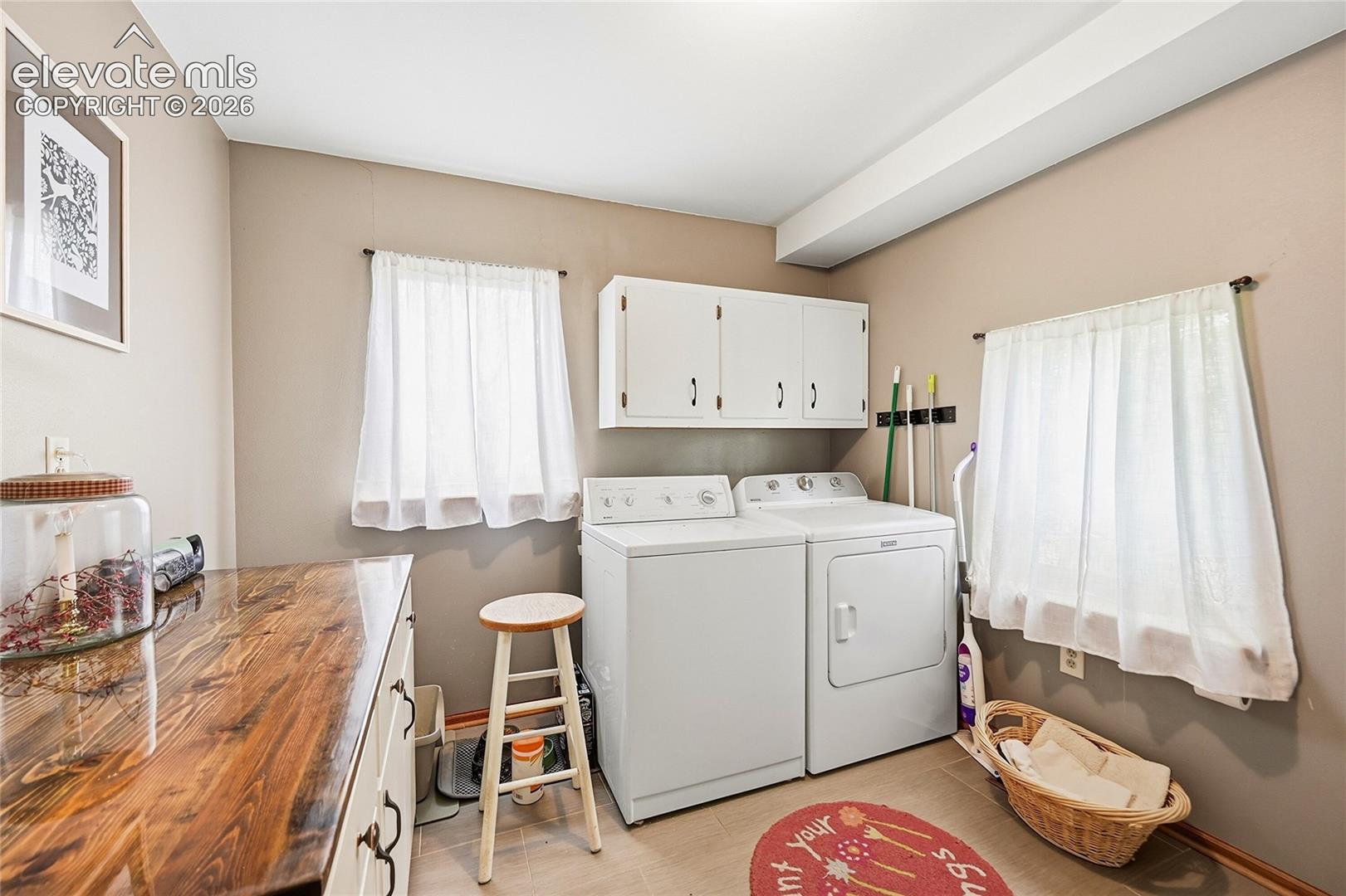 Laundry area featuring tile flooring, built-in white upper cabinetry, and a countertop with a natural wood finish